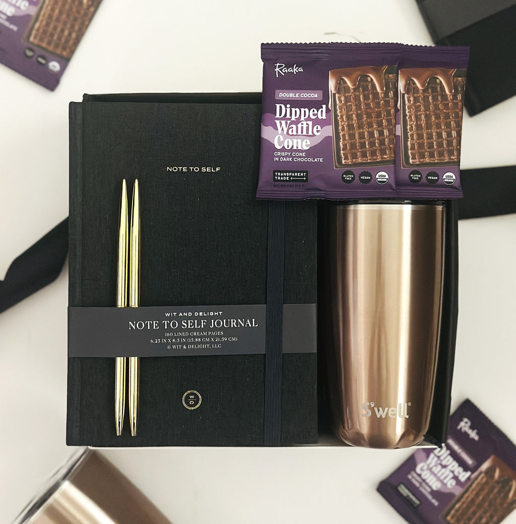 Gift set with a black journal, rose gold tumbler, and waffle cone packets on a white background.