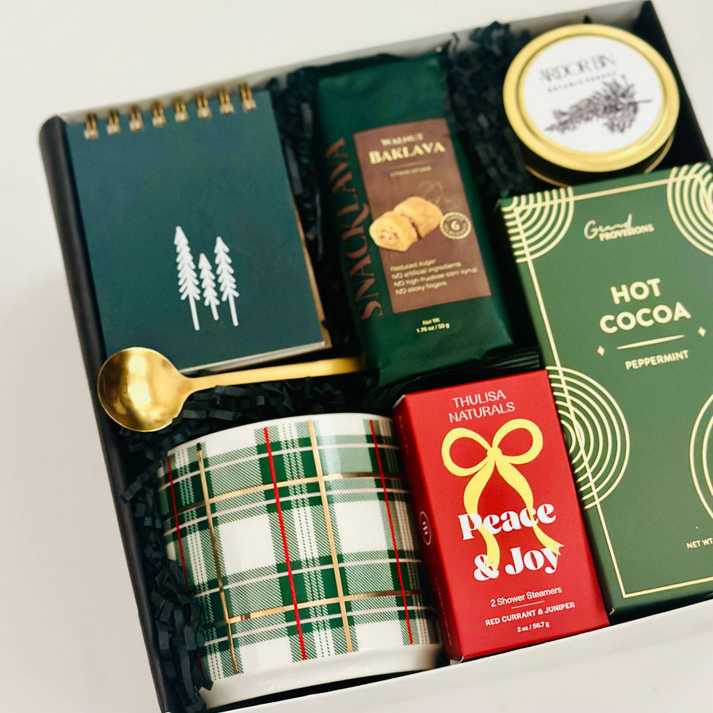Holiday gift set with a mug, hot cocoa mix, and other items in a box.