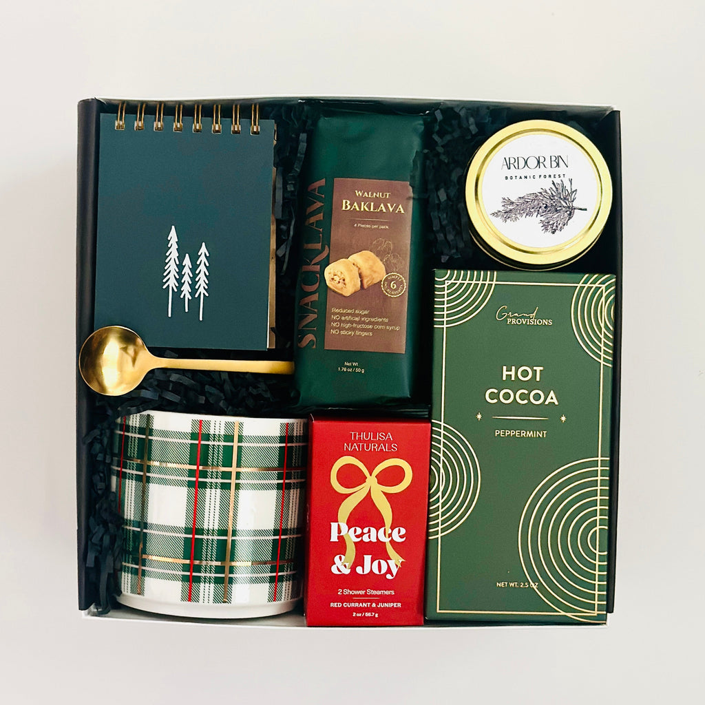 Gift set with a notebook, hot cocoa mix, and other items in a box on a white background