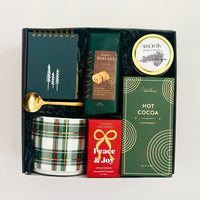Gift set with a notebook, hot cocoa mix, and other items in a box on a white background