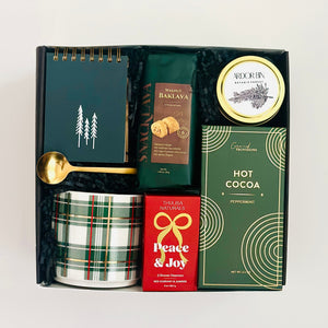 Gift set with a notebook, hot cocoa mix, and other items in a box on a white background