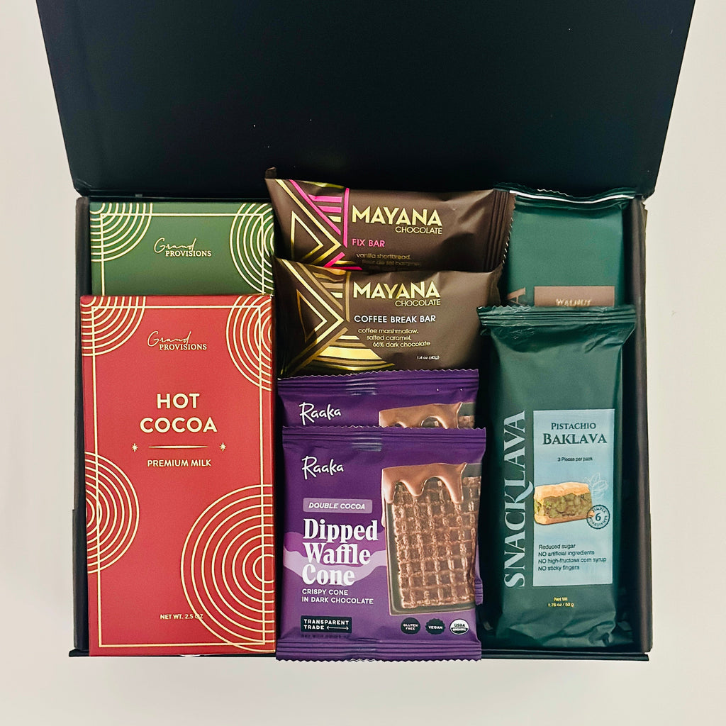 Assorted snacks including hot cocoa mix, waffle cone bites, and baklava in a black box on a white background.